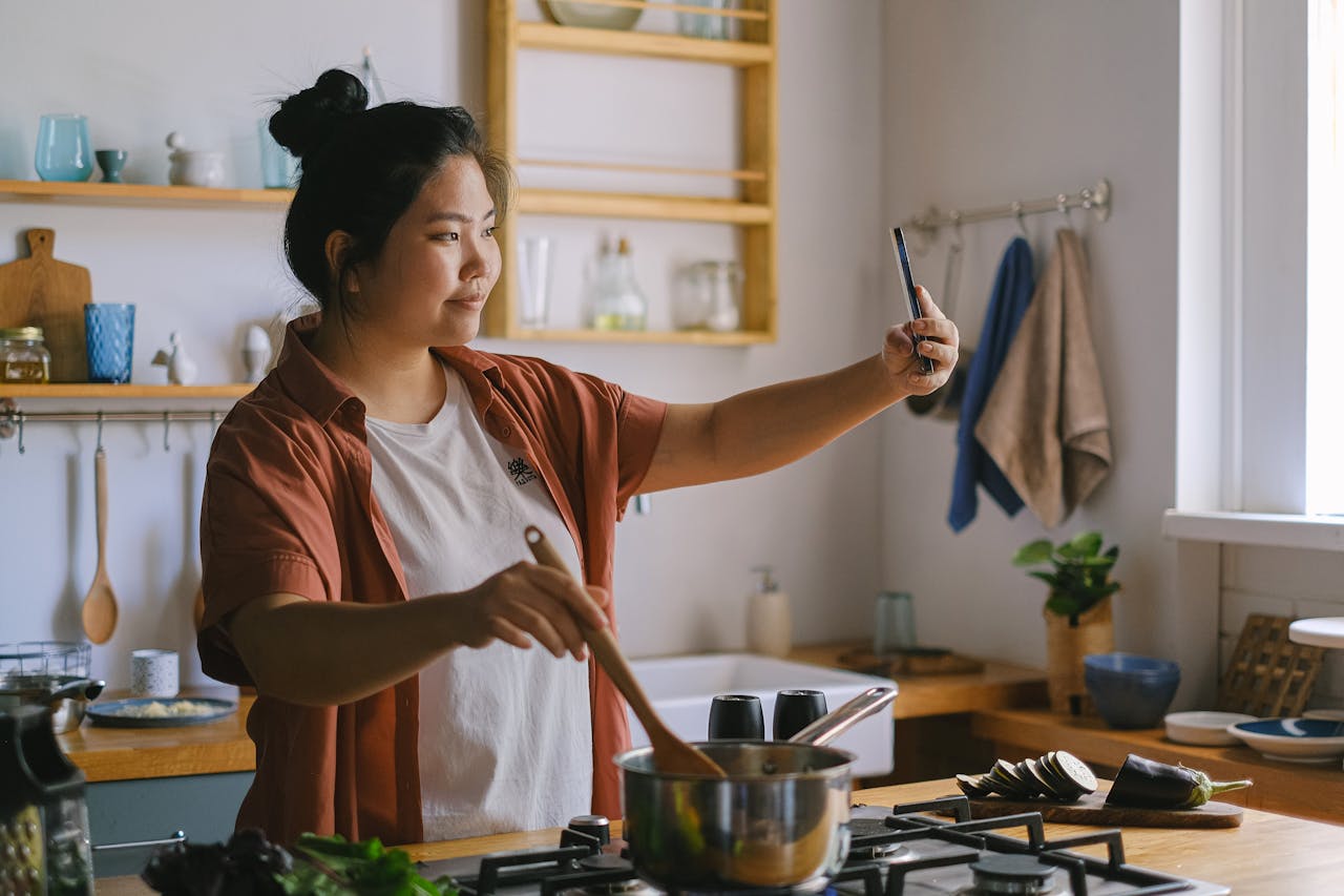 our-story Woman cooking in kitchen and taking selfie, capturing the moment.